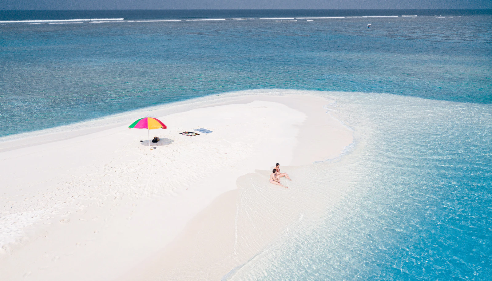 A beach umbrella and guests on a bright white Maldives sandbank