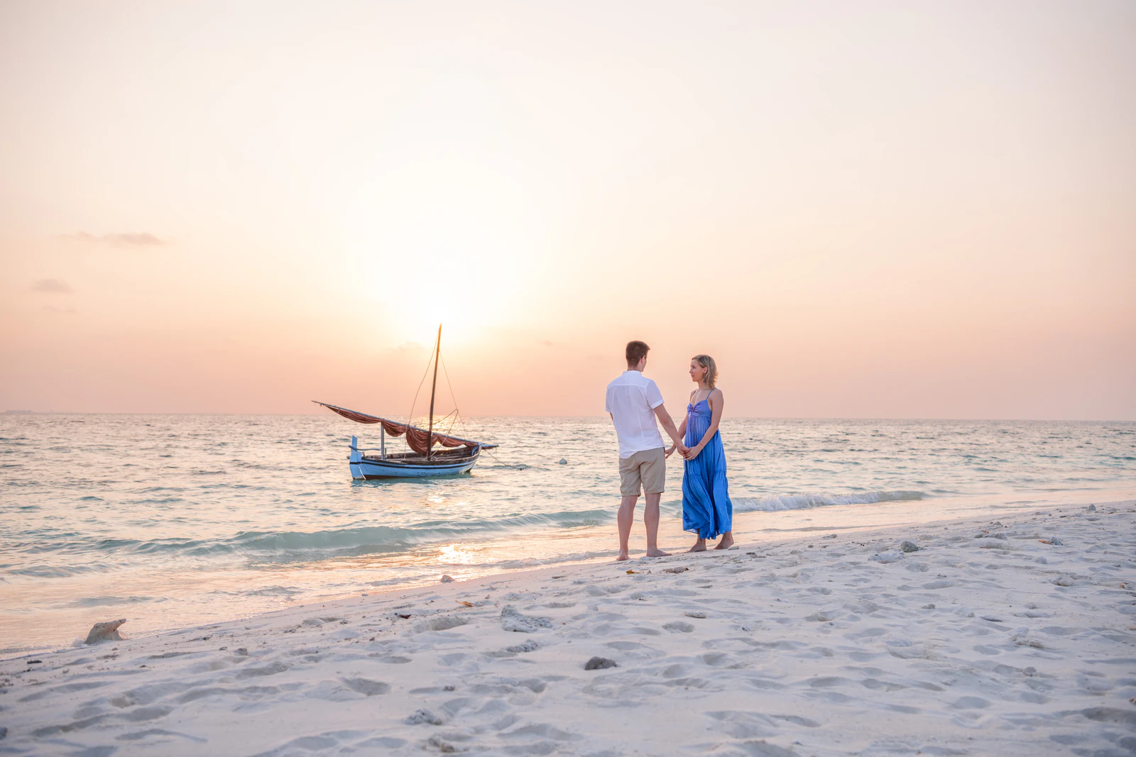 A couple on the beach at sunset beside a traditional dhoni offshore