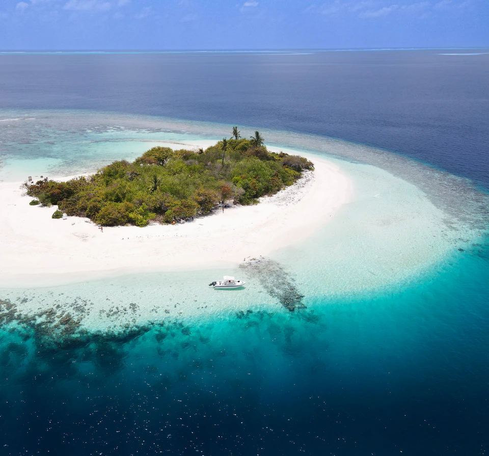 Aerial view of a small uninhabited island, lagoon, and boat