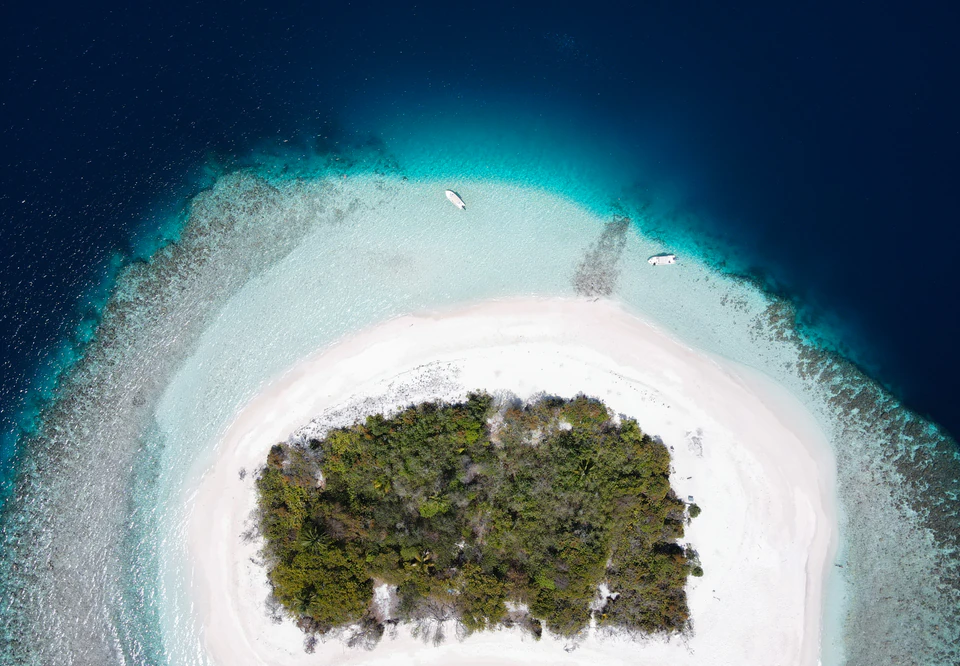 Top-down aerial view of a small island encircled by white sand and lagoon