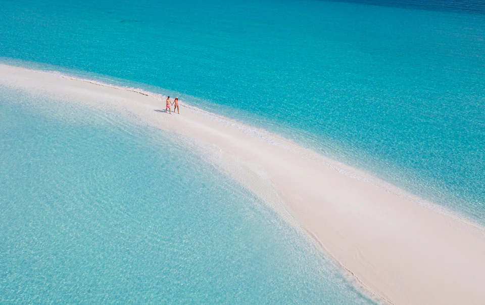 Aerial view of a couple walking on a long sandbank in turquoise water