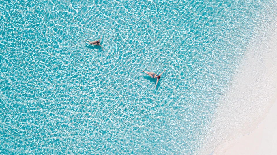 Top-down view of two swimmers beside a white sandbank
