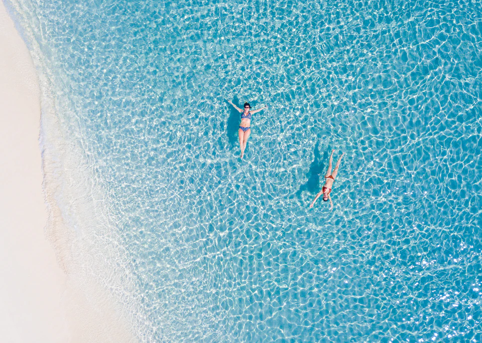 Vertical top-down view of two swimmers in clear lagoon water
