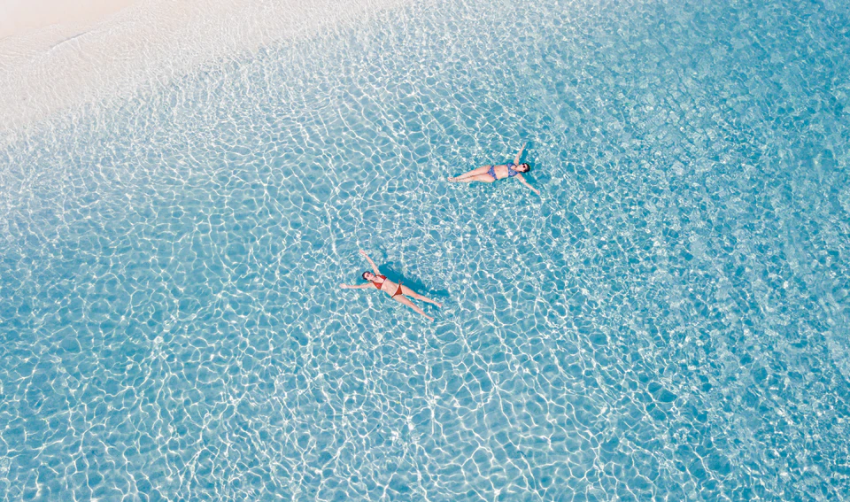 Wide top-down view of two swimmers beside the sand edge