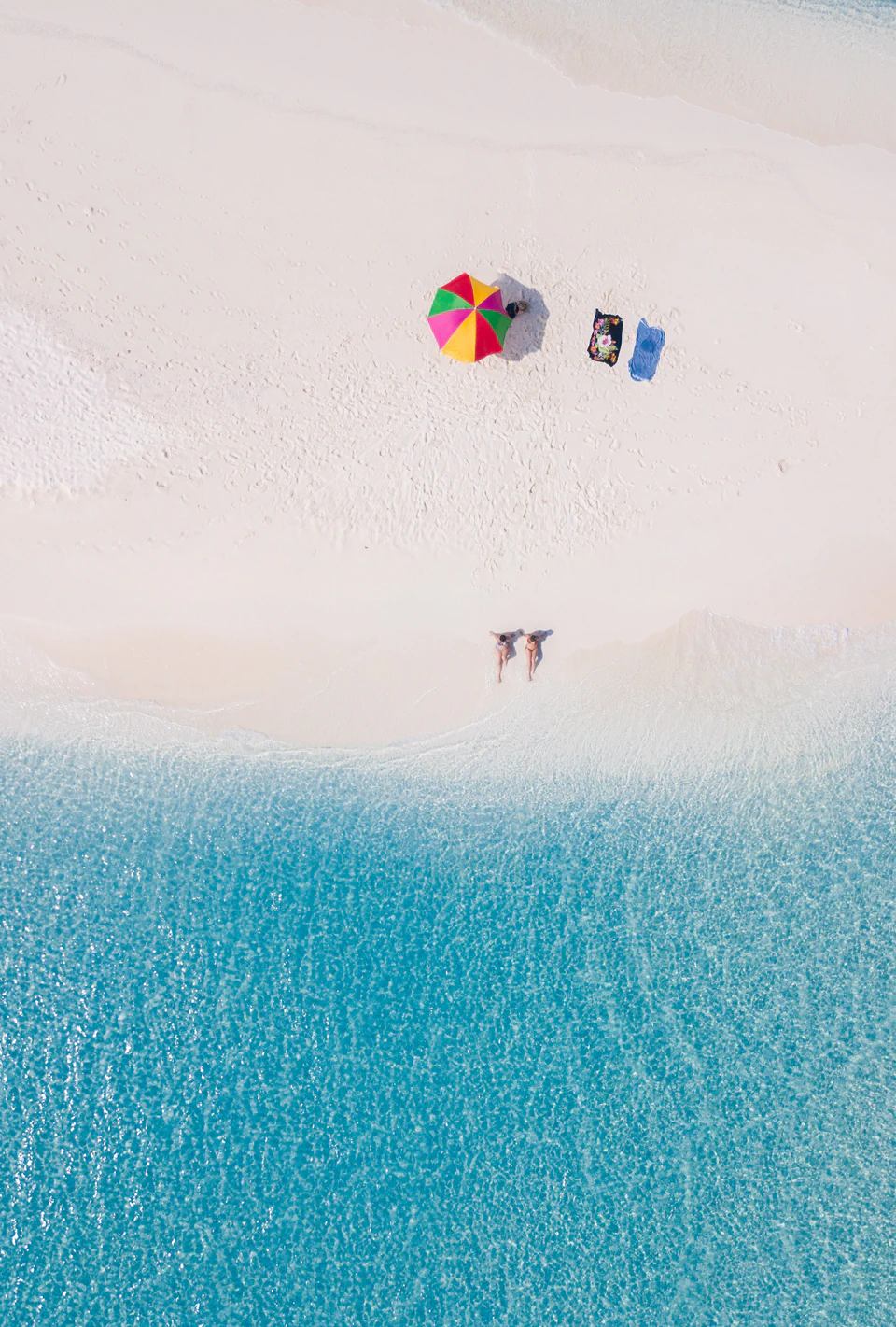 Top-down sandbank scene with an umbrella and guests at the waterline